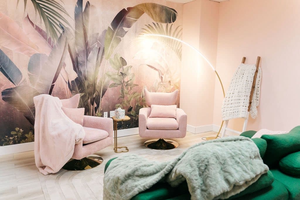 A counseling room with pink chairs, botanical wall art, and a gold floor lamp.