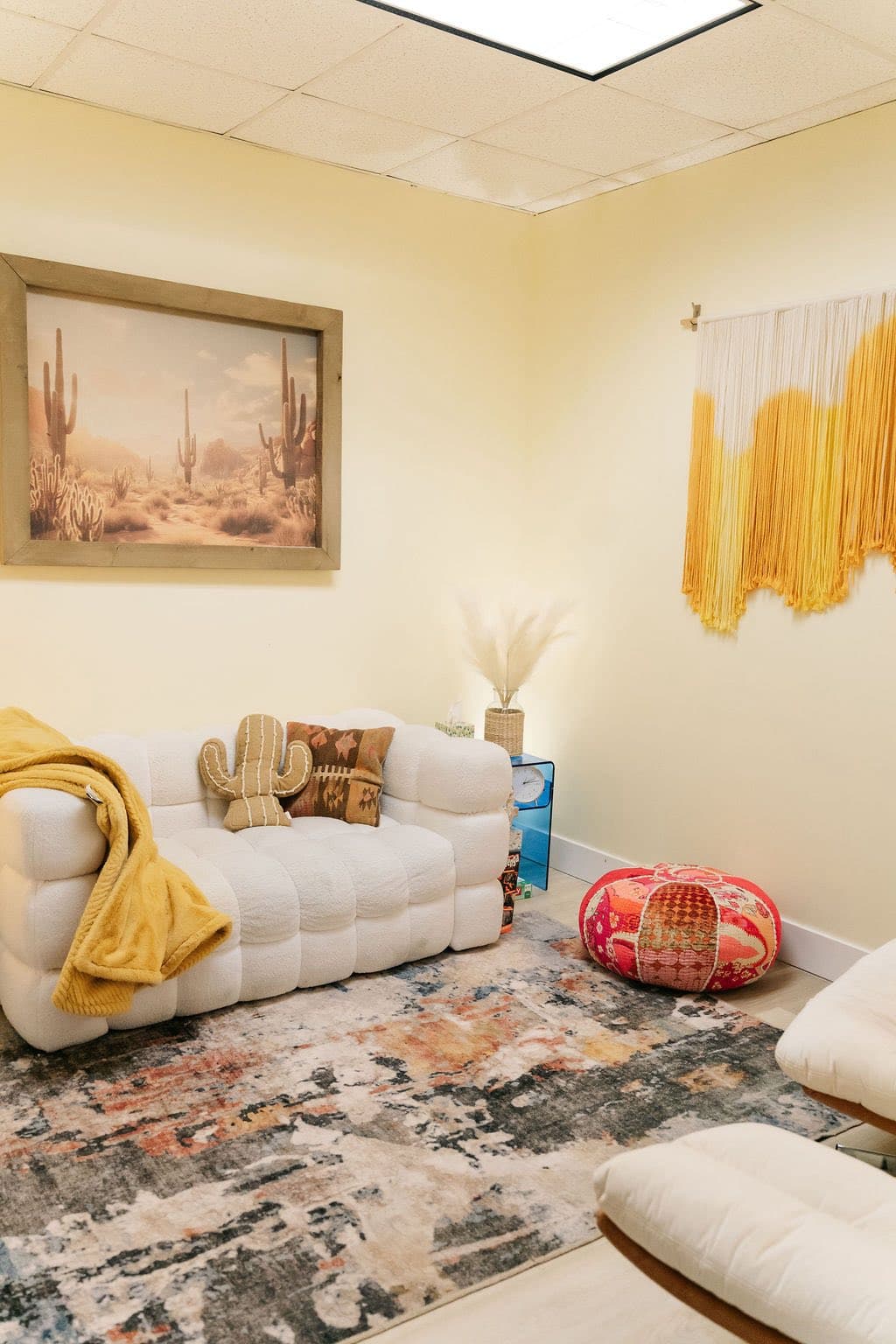 A counseling room with a white sofa, desert-inspired decor, and a macrame wall hanging.