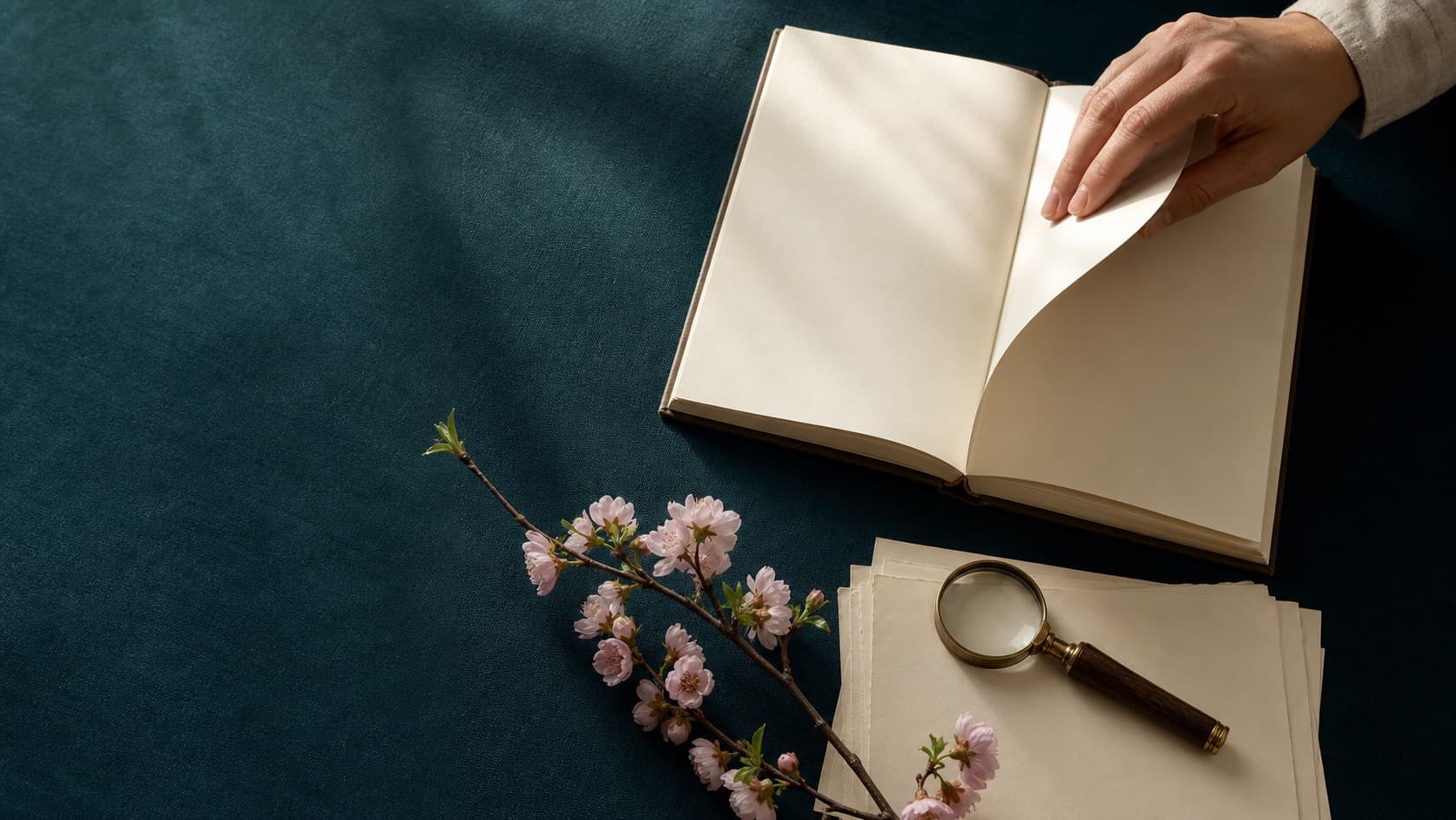 A hand turning an unmarked book beside research papers and a cherry branch