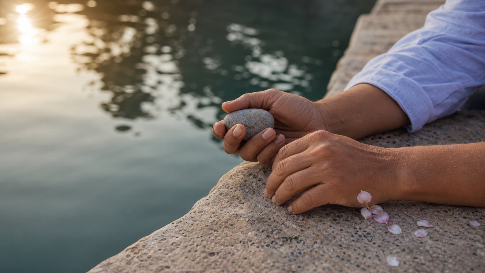 Hands holding a smooth river stone beside quiet water